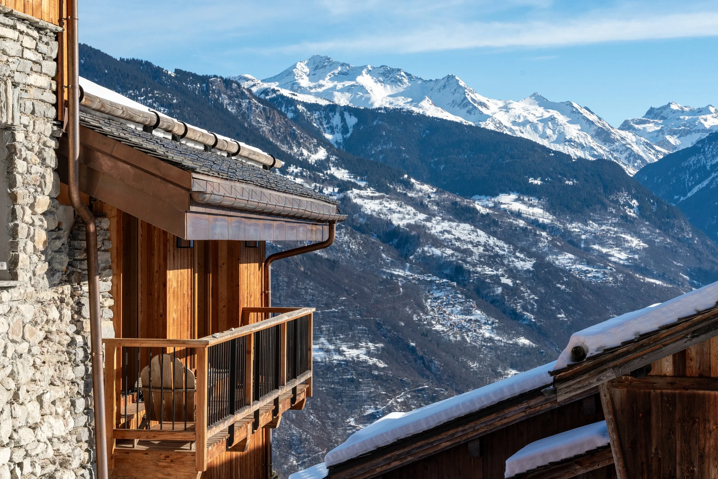 Snow-covered Alpine mountains and valley viewed from a rustic stone-and-wood chalet balcony