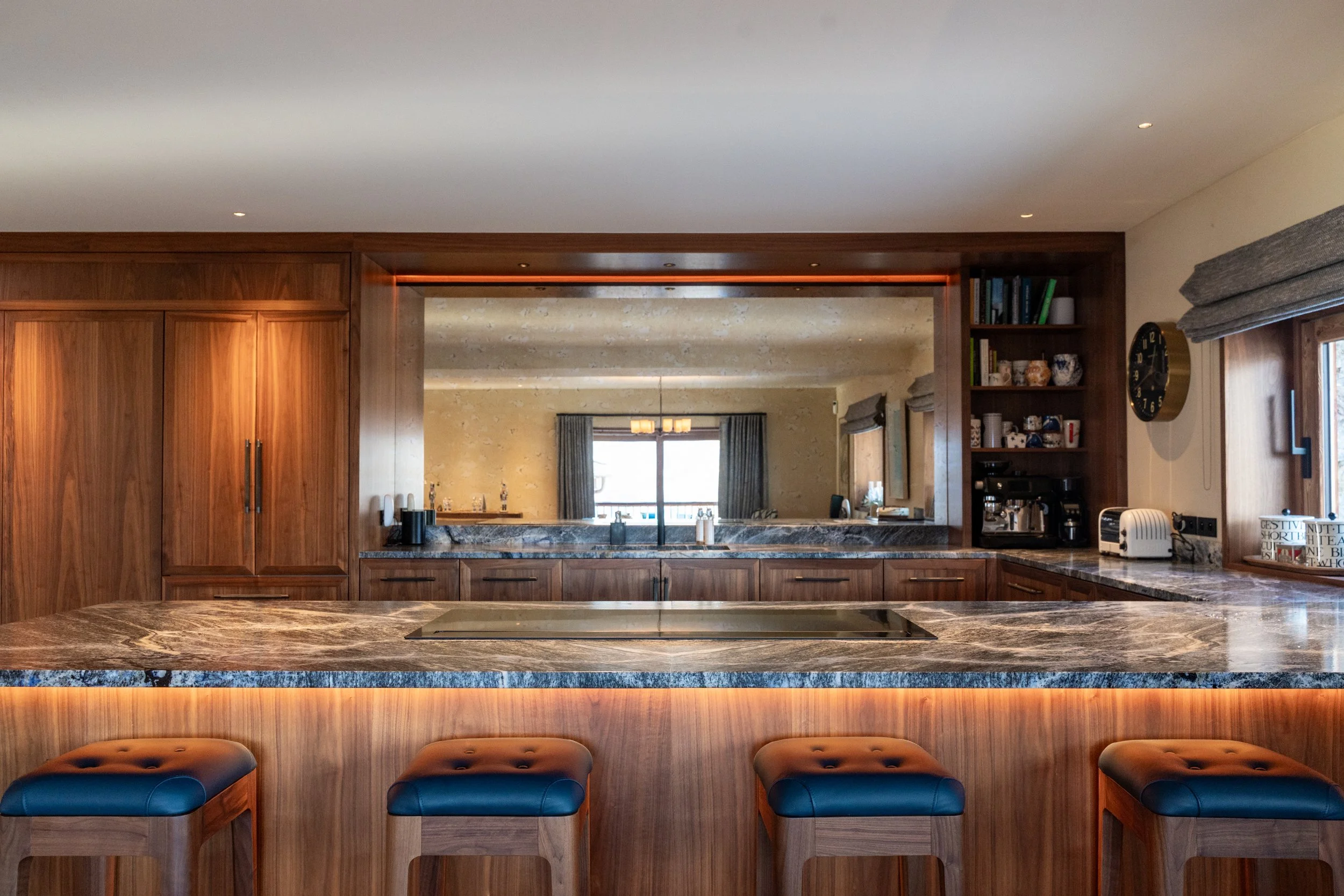 Luxury home bar with walnut cabinetry, marble countertop, built-in cooktop, open shelving, coffee station, and four blue leather bar stools