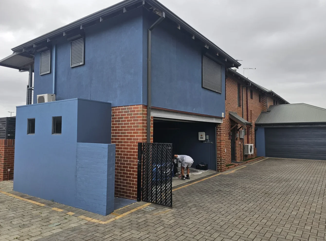 Before repainting: two-storey house with blue-grey walls, exposed brickwork and a garage.