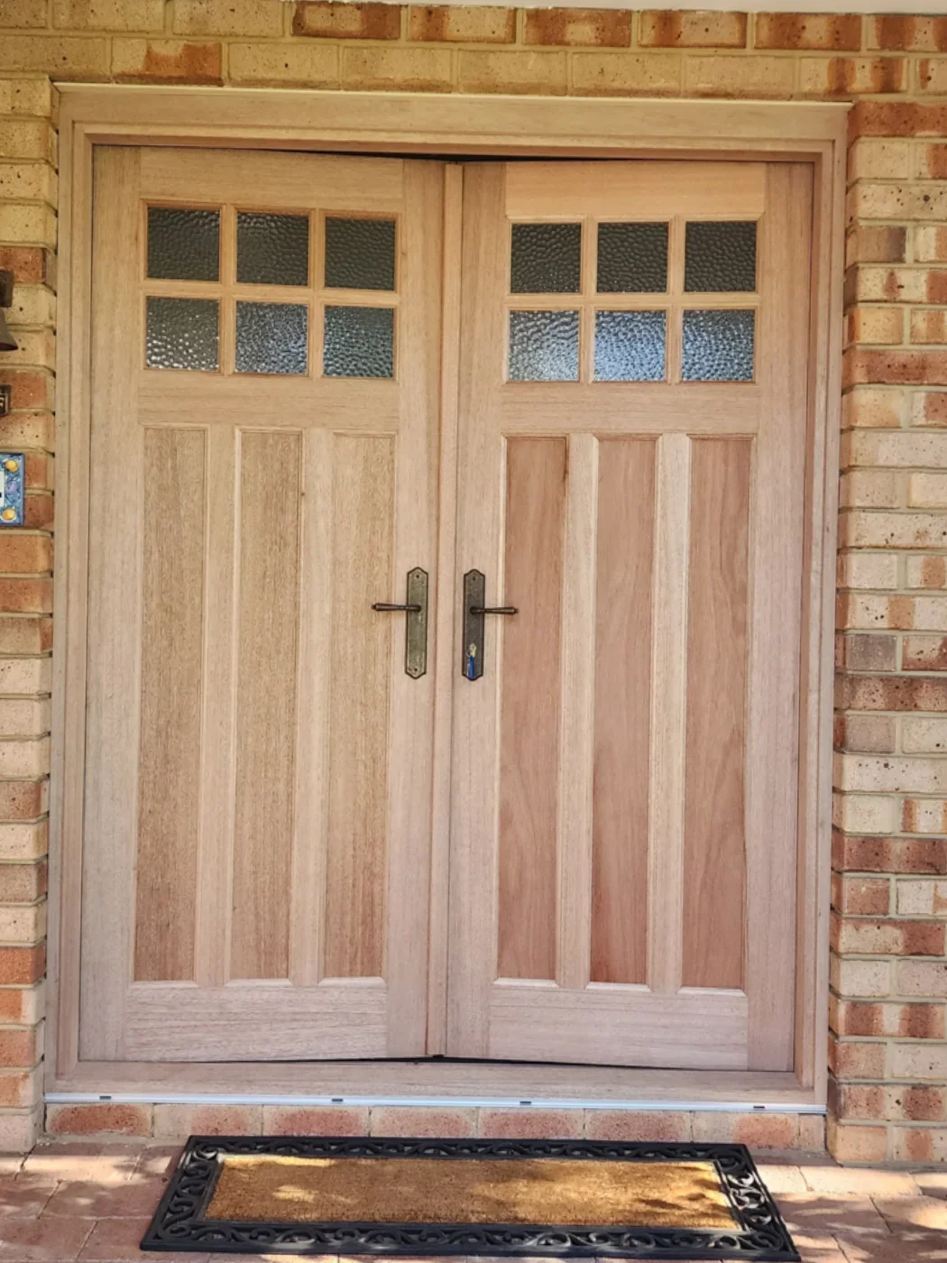 Before repainting: natural timber double entrance doors and frame set in a brick wall.