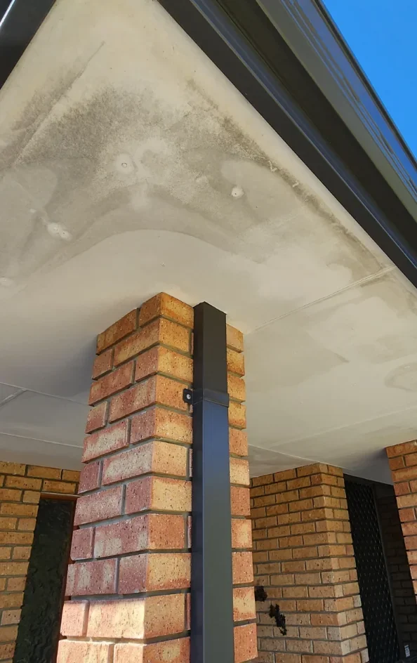 Before repainting: patched soffit above brick columns at a covered entrance.