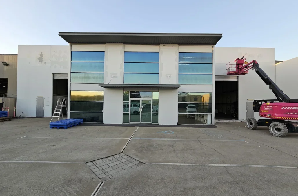 Before repainting: commercial building with pale facade panels and light blue upper window sections.