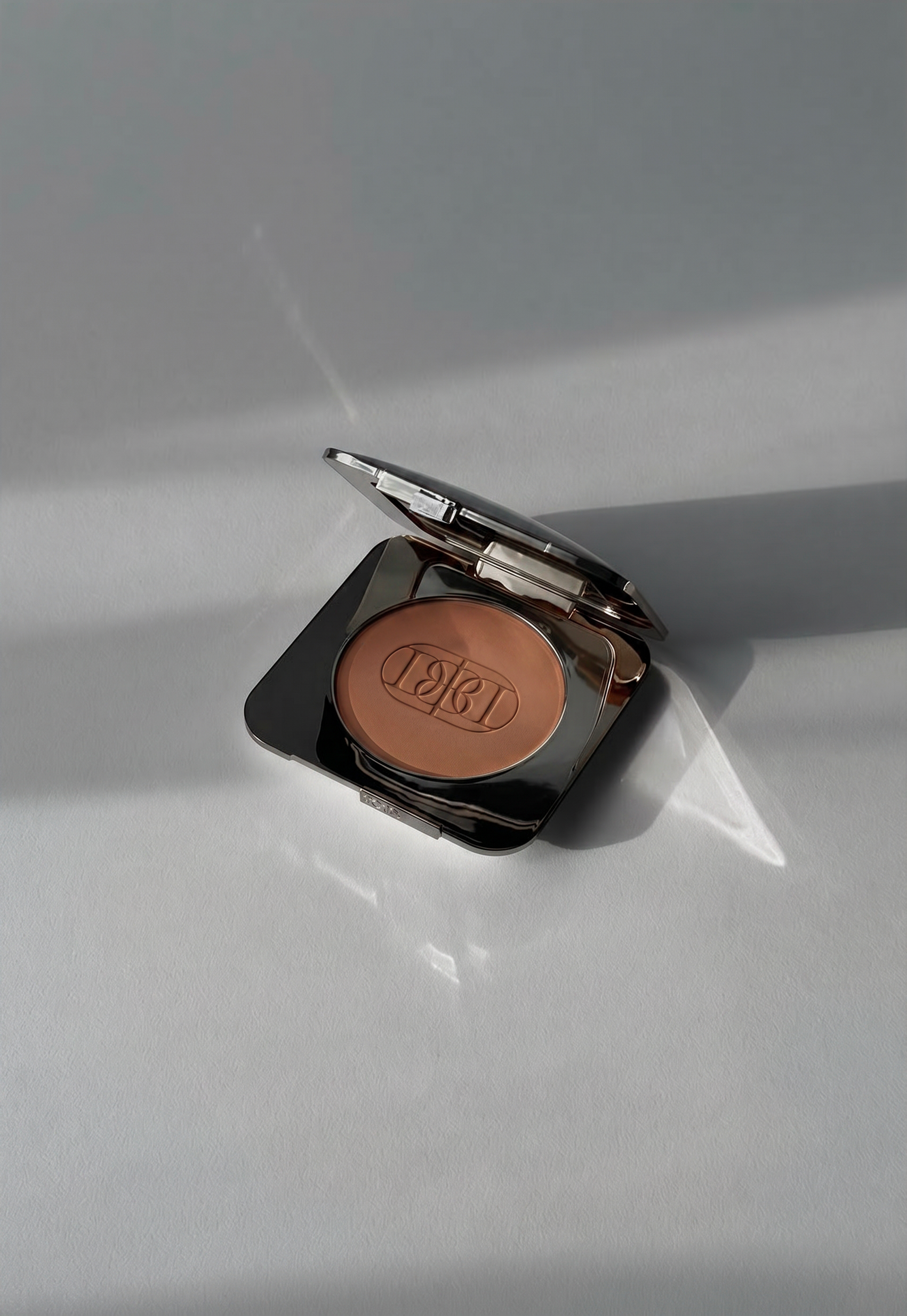 Pressed powder makeup compact photographed in natural sunlight with the Domenica Beauty logo.