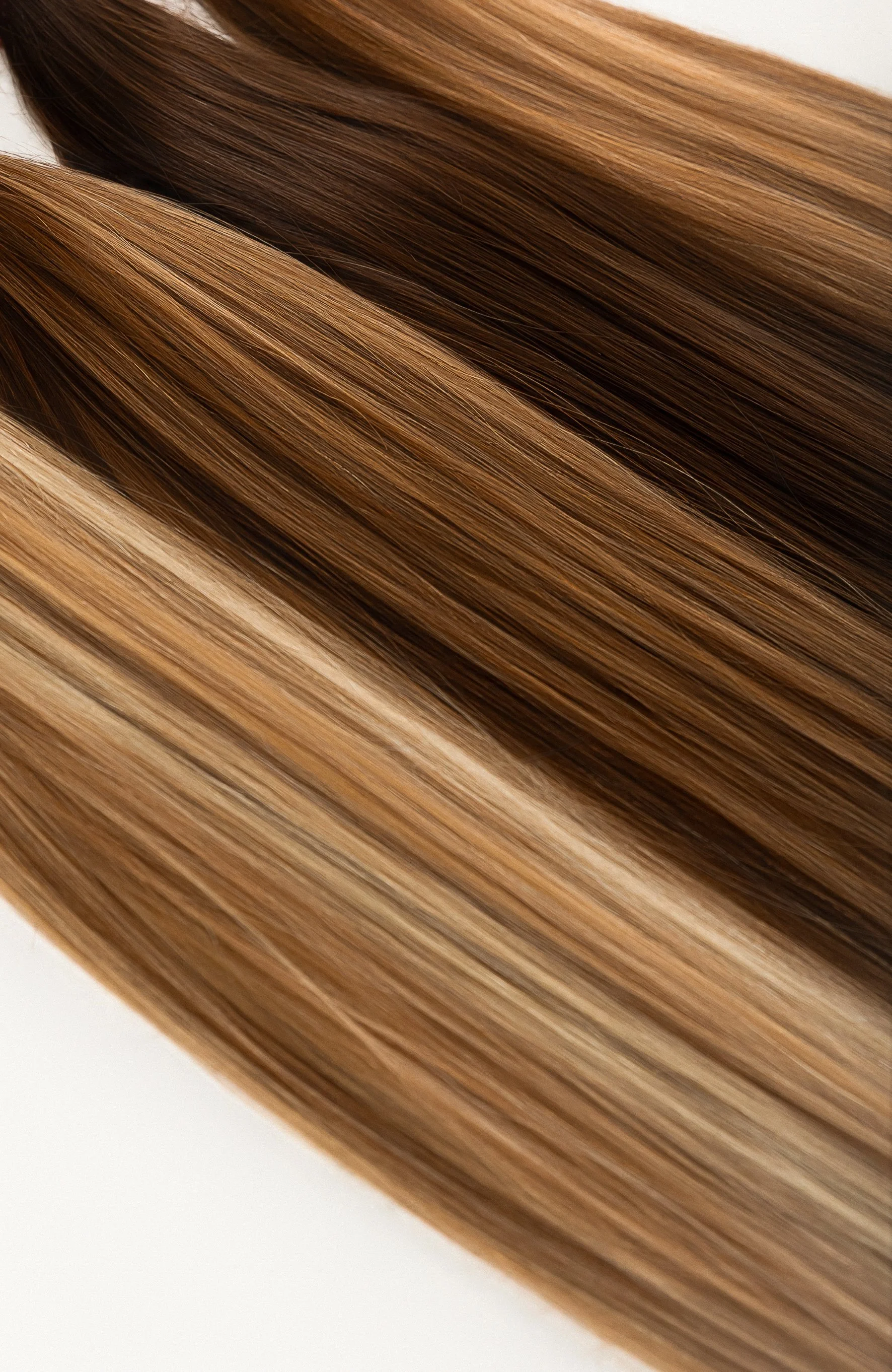 Close-up of long brunette custom hair extensions with dimensional blonde highlights and smooth styling.