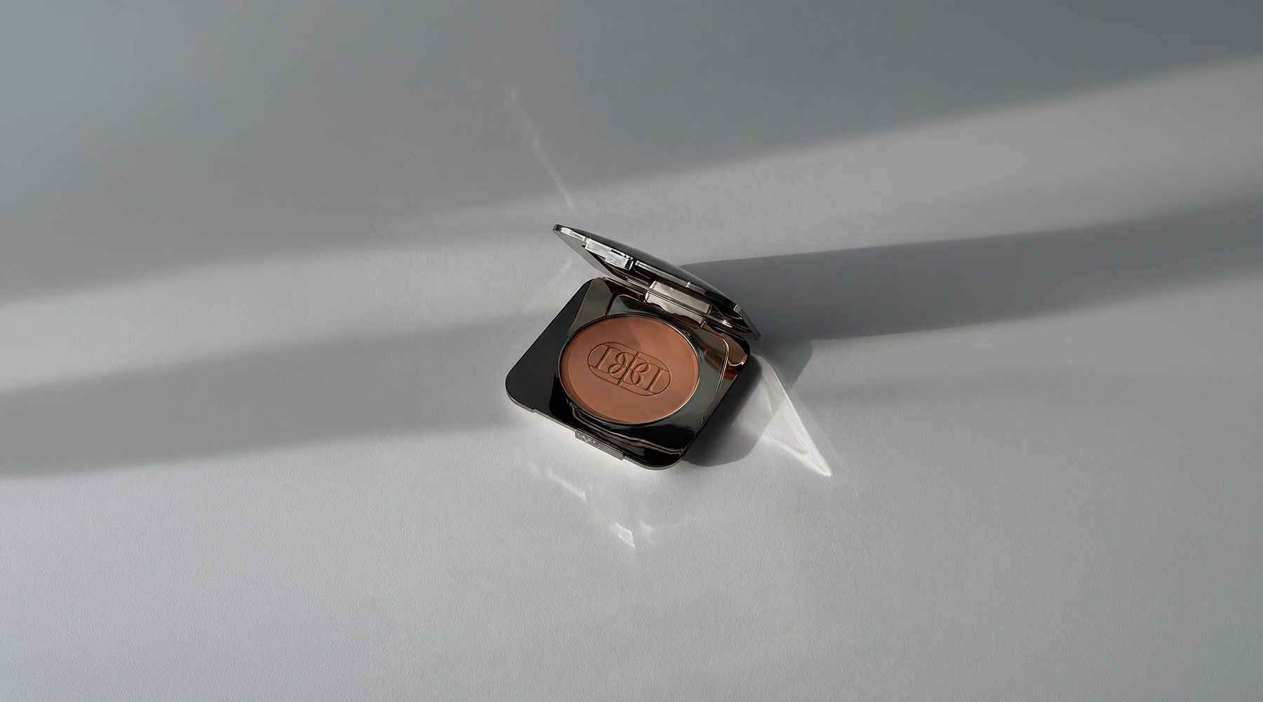 Pressed powder makeup compact photographed in natural sunlight with Domenica Beauty logo.