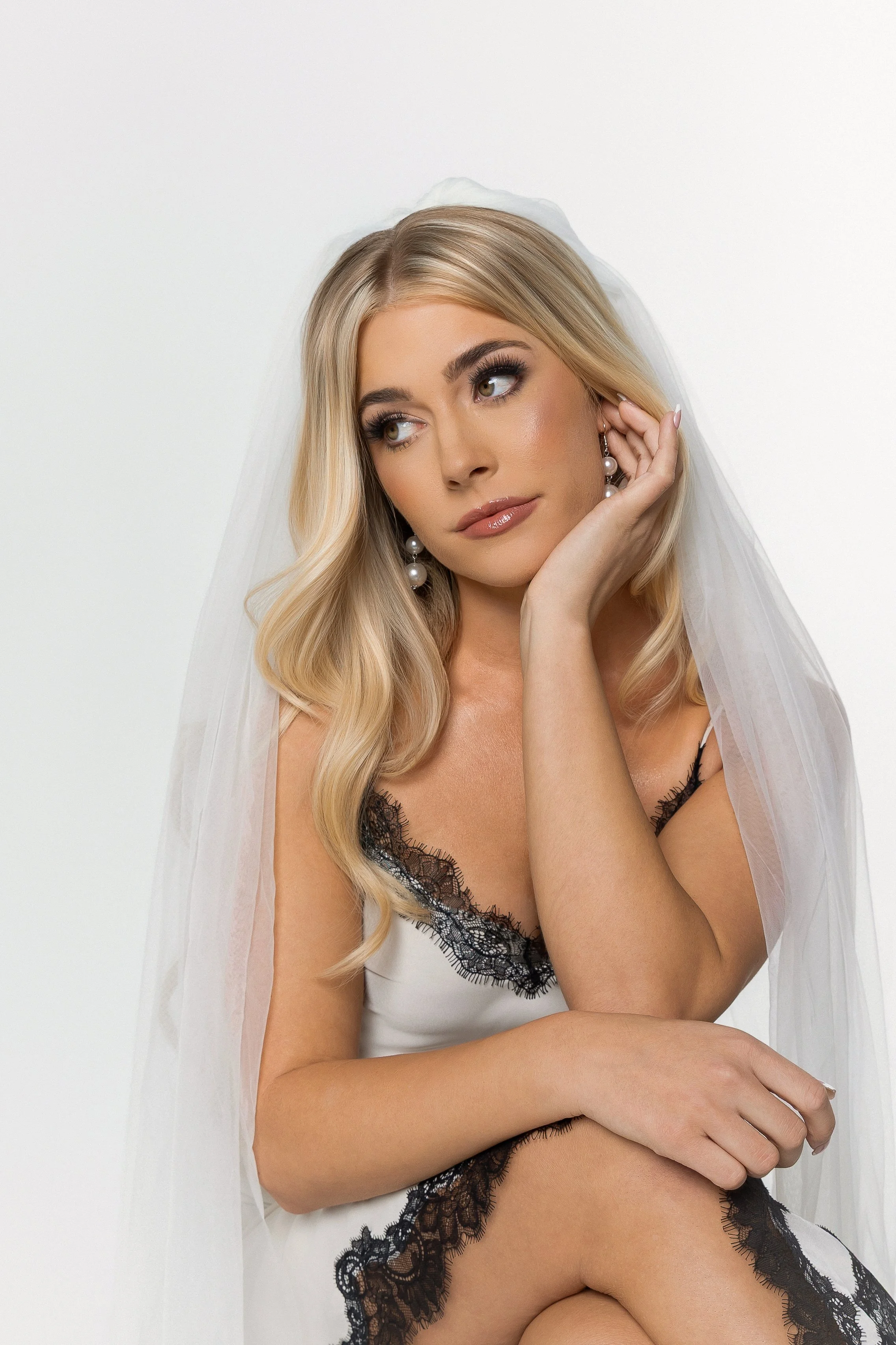 Bridal hair and makeup look with long blonde waves, a white robe, and wedding veil.