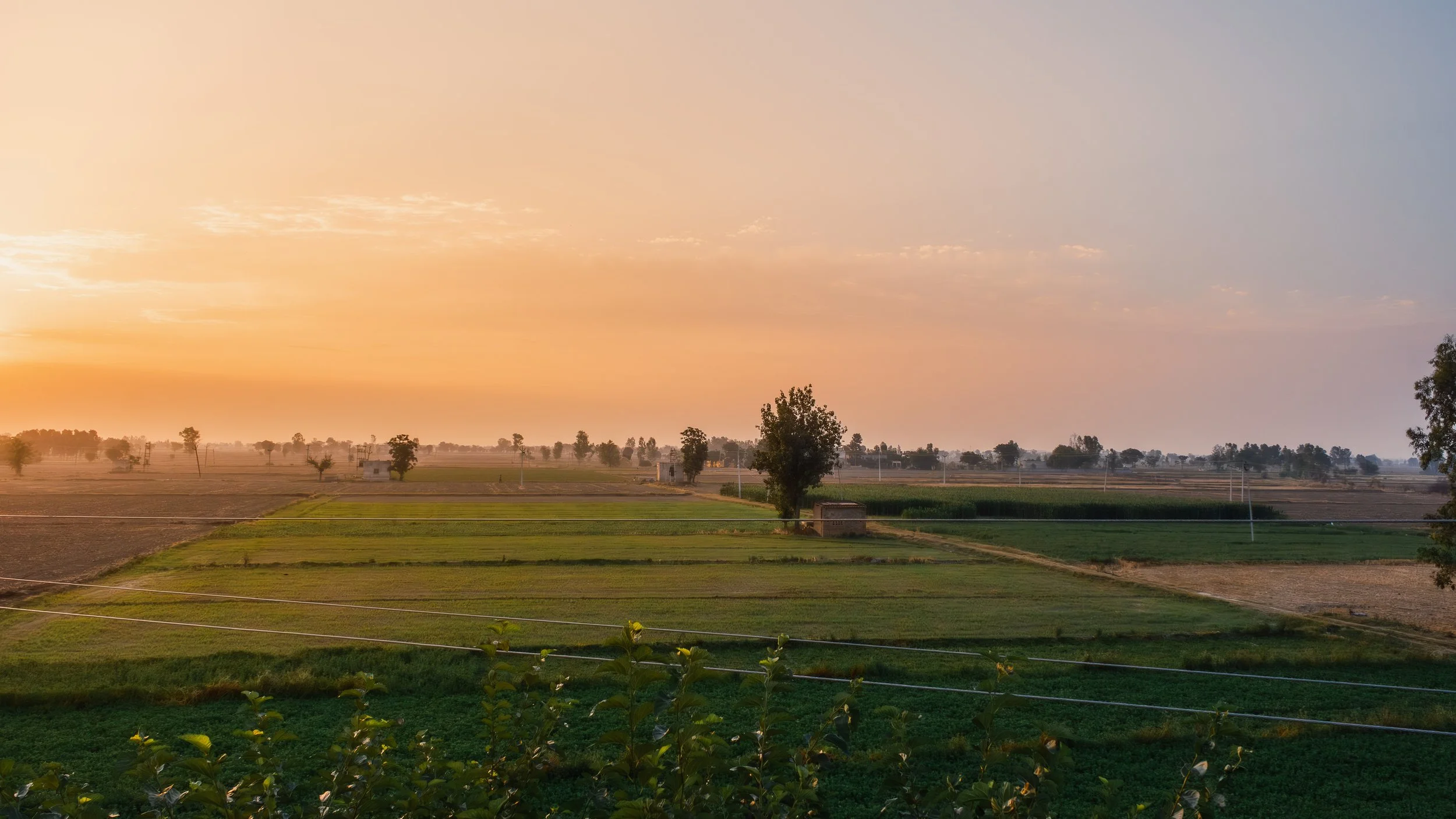 Sunset over a rural landscape with fields, trees, and scattered small buildings.