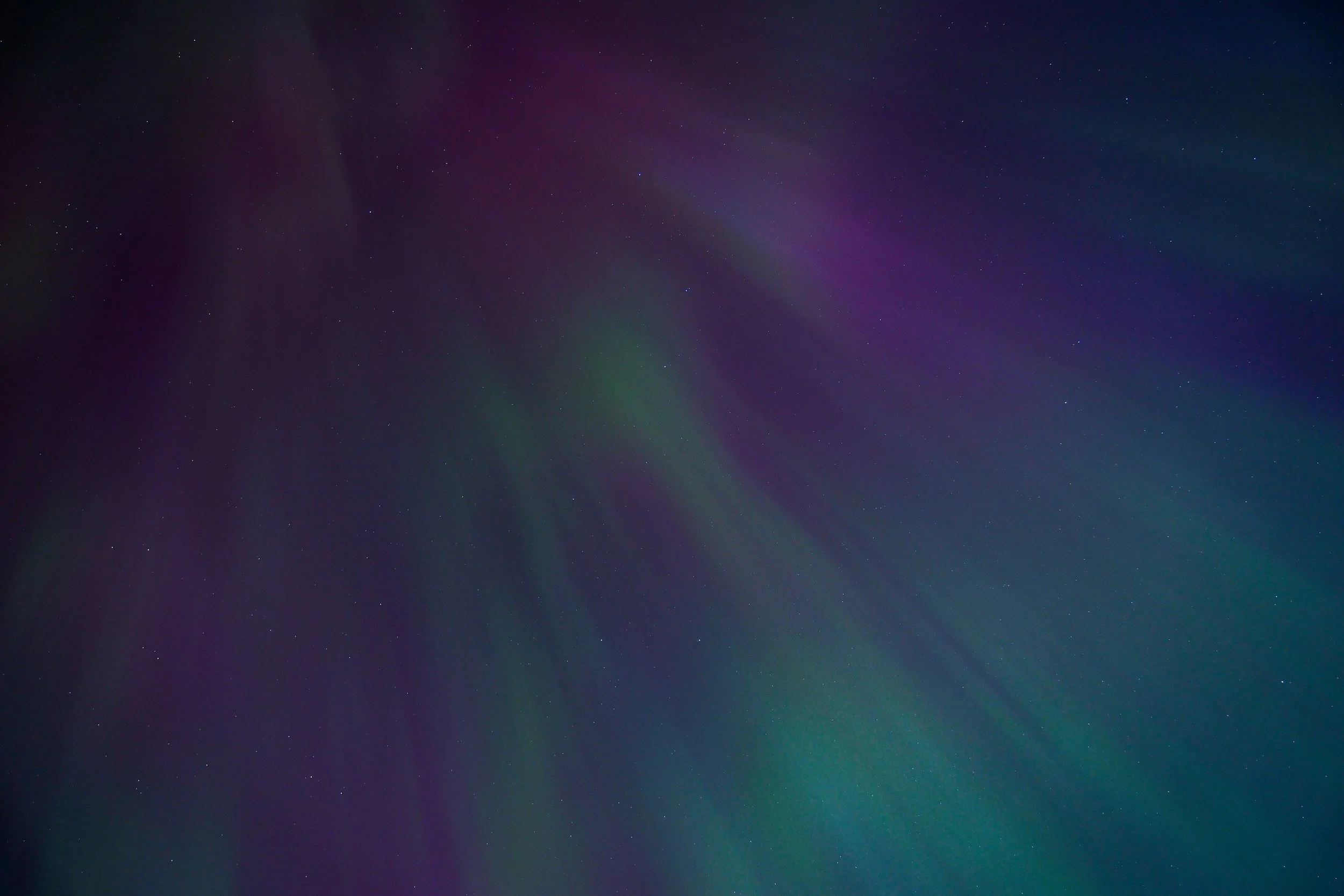 Night sky with scattered stars and faint colorful aurora borealis.