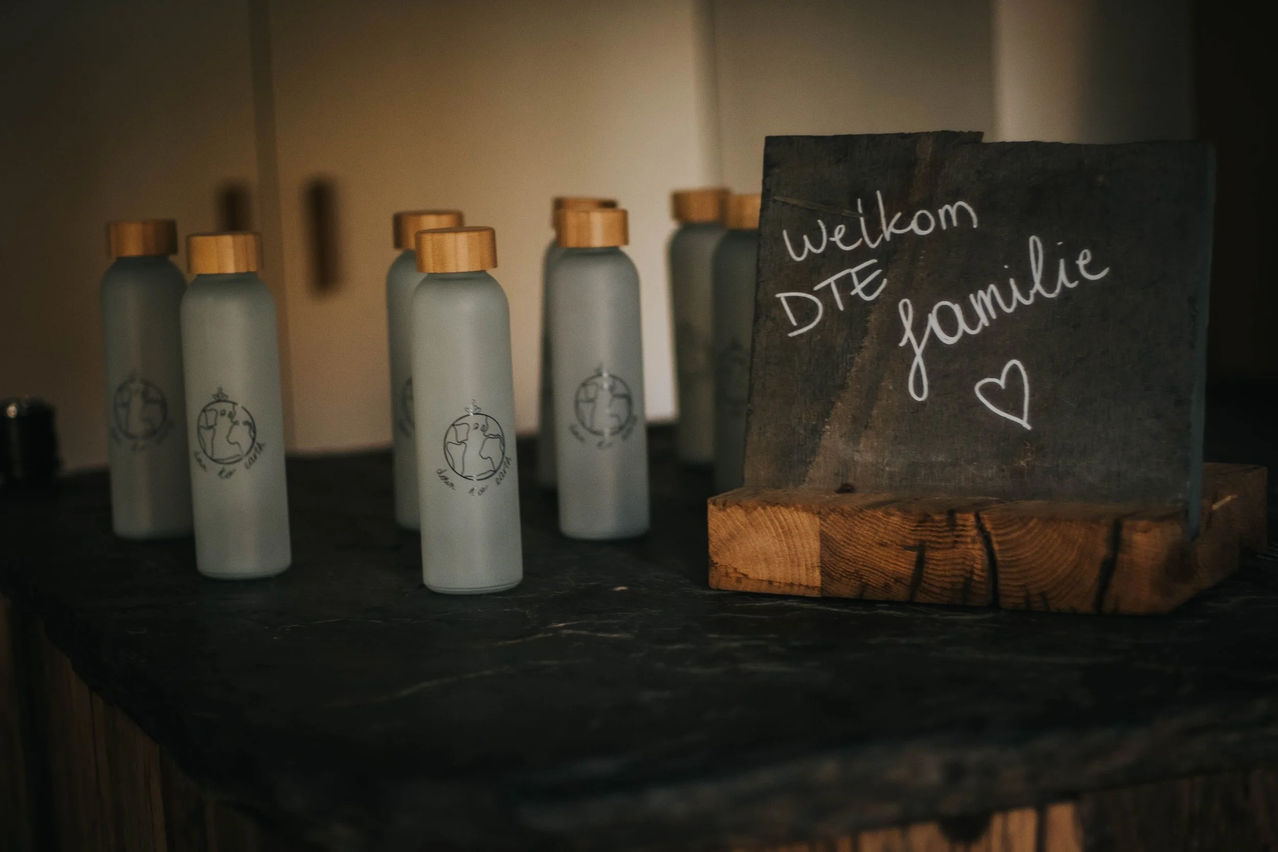 Row of white bottles with wooden caps and a wooden block with handwritten sign that says 'Welkom DTE familie' and a heart symbol.