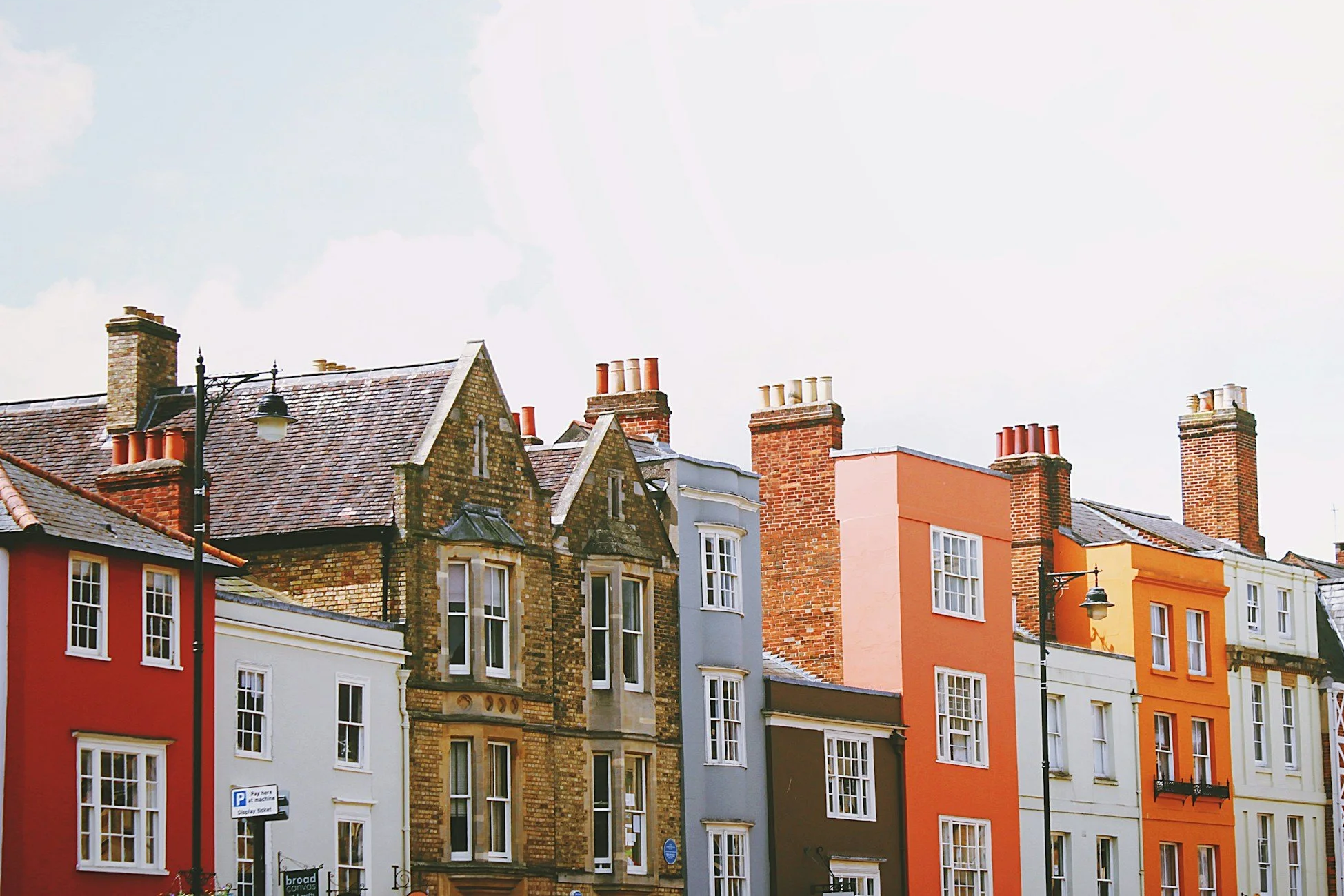 Colorful multi-story buildings with traditional brickwork and modern facades, topped with numerous chimneys, under a light cloudy sky.