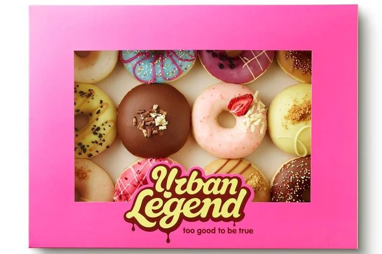 Assorted colorful donuts with various frostings and toppings inside a pink box labeled "Urban Legend - too good to be true."