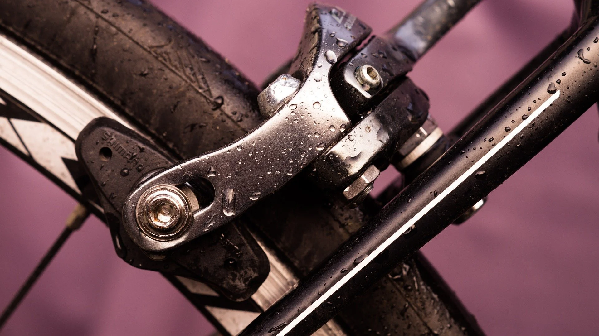 Close-up of a wet bicycle handlebar with water droplets, showing the head tube and part of the front fork against a purple background.