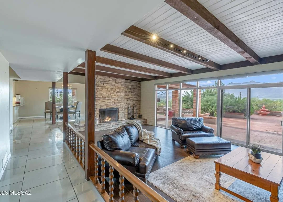 Living room with brown leather sofas, a stone fireplace, large sliding glass doors leading to an outdoor patio, and a dining area in the background.