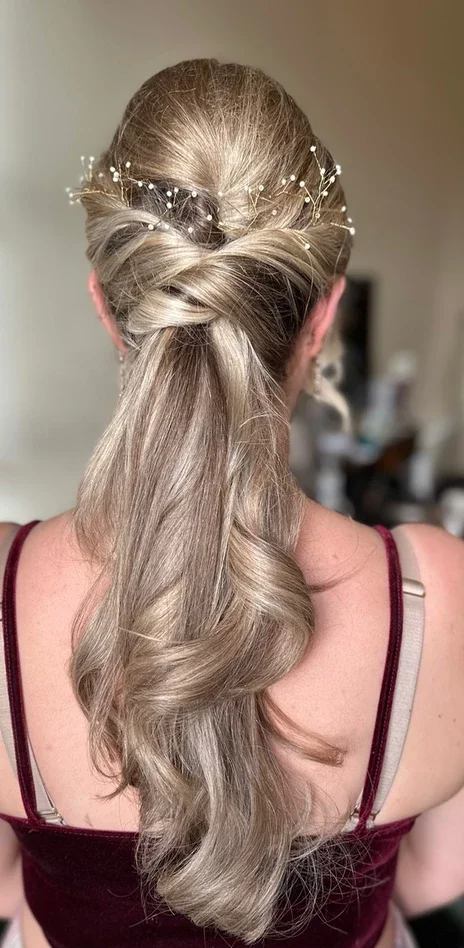 Claire Field Bridal Hair and Make up. Back of woman's head with styled long blonde hair in loose waves, adorned with a decorative hairpiece with small white pearls.