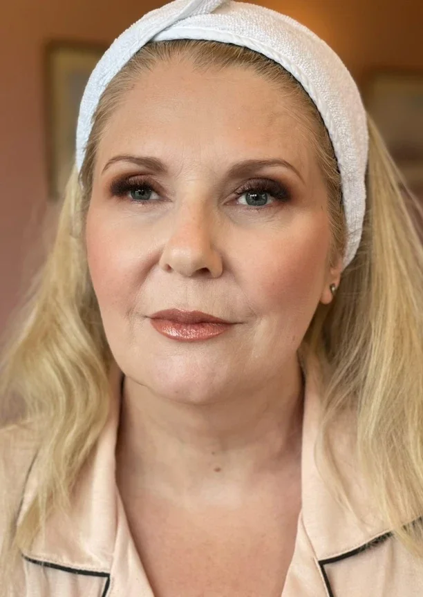 Claire Field Bridal Hair and Make up. Portrait of a woman with blonde hair wearing a white headband, makeup, and a light-colored shirt with black piping.