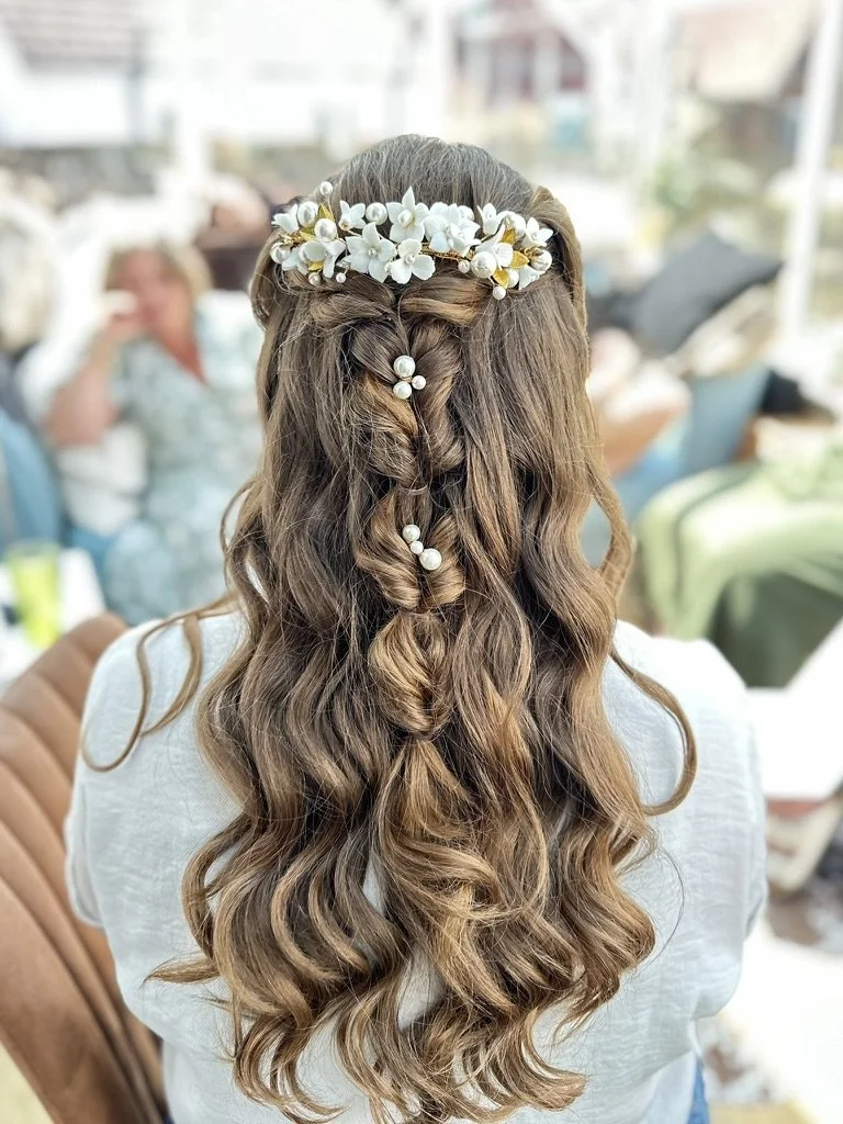 Claire Field Bridal Hair and Make up. Woman with long, curly hair wearing a floral crown with white flowers and pearls, seen from behind.