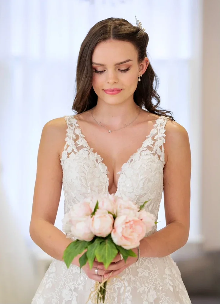 Claire Field Bridal Hair and Make up. A woman in a white lace wedding dress holding a bouquet of pink peonies.