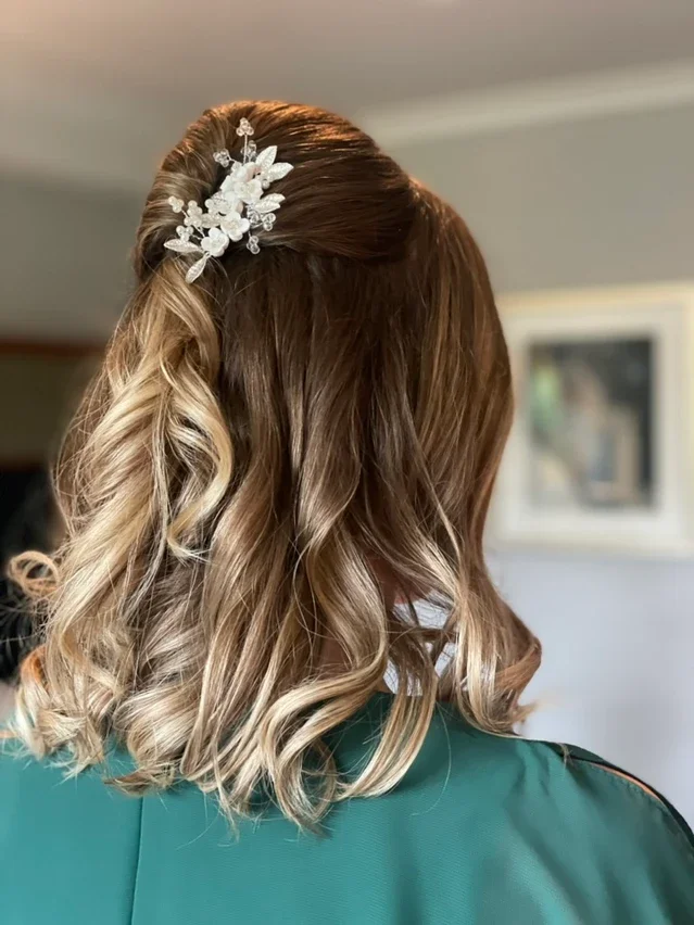 Claire Field Bridal Hair and Make up. Close-up of a woman's hairstyle with loose curls and a decorative white floral hair accessory.