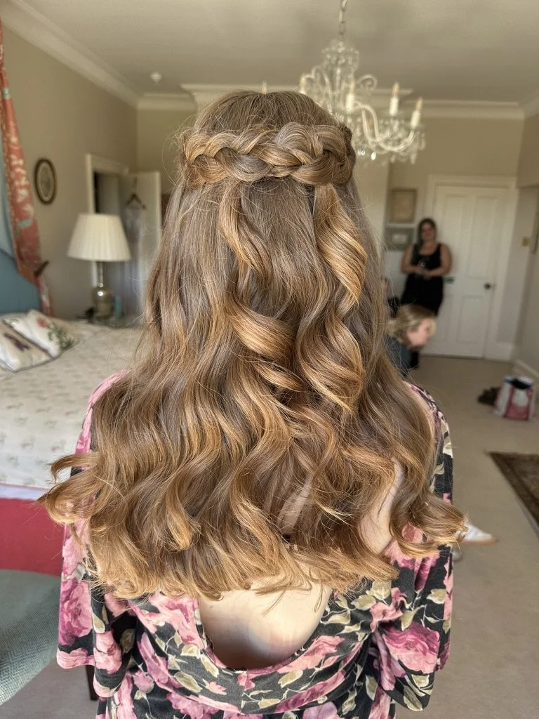 Claire Field Bridal Hair and Make up. Rear view of a woman with long, wavy, light brown hair styled with a braid crown across the top of her head.