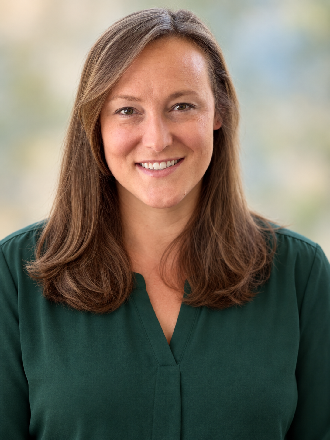 Dr. Elisha N. Gulledge with long brown hair smiling at the camera, wearing a dark green top, with a blurred outdoor background.