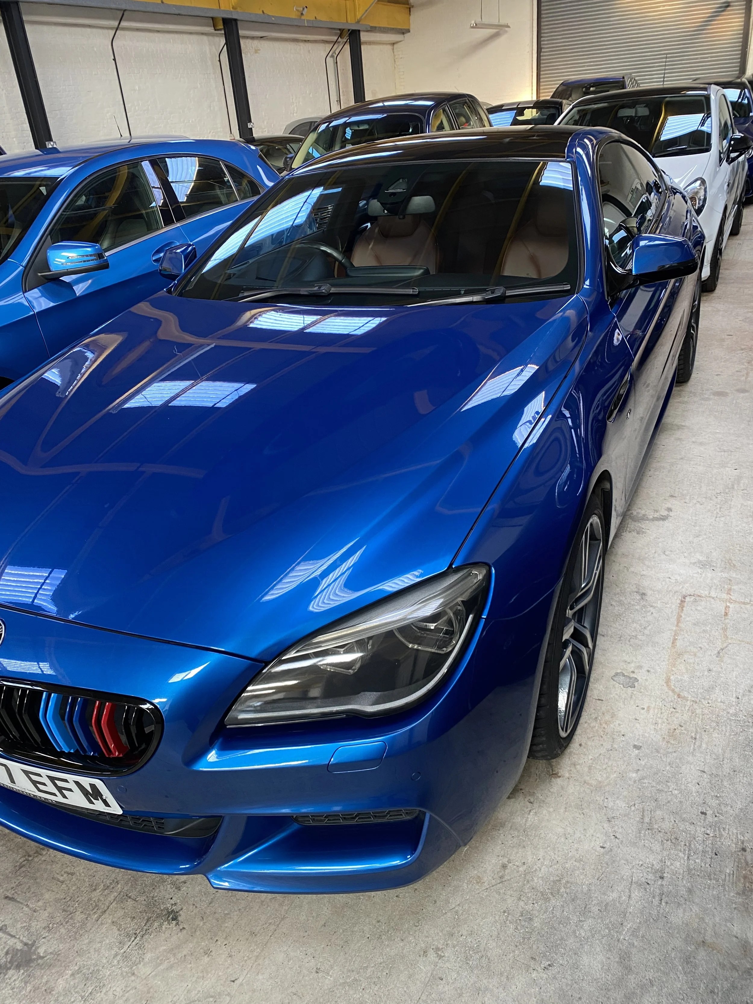A shiny blue sports car with black accents parked indoors, surrounded by other vehicles.