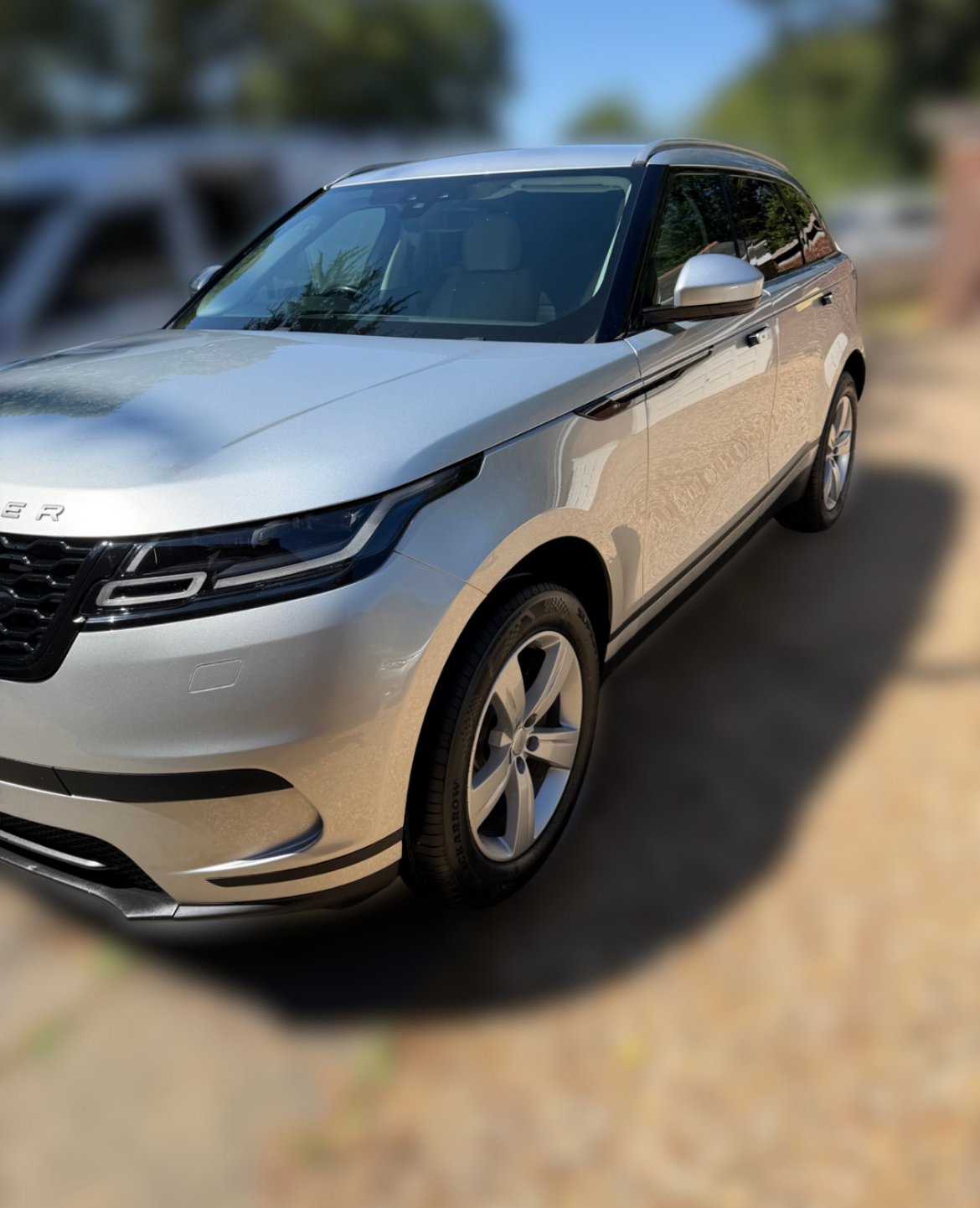 Silver SUV parked outdoors on a sunny day, with a blurred background of trees and other vehicles.