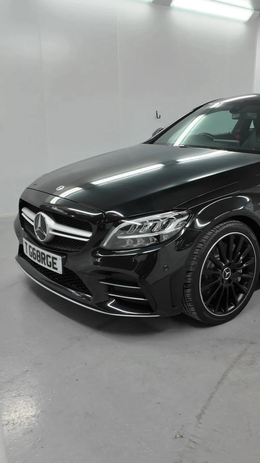 A black Mercedes-Benz sports car in an indoor parking garage with white walls and fluorescent lighting.
