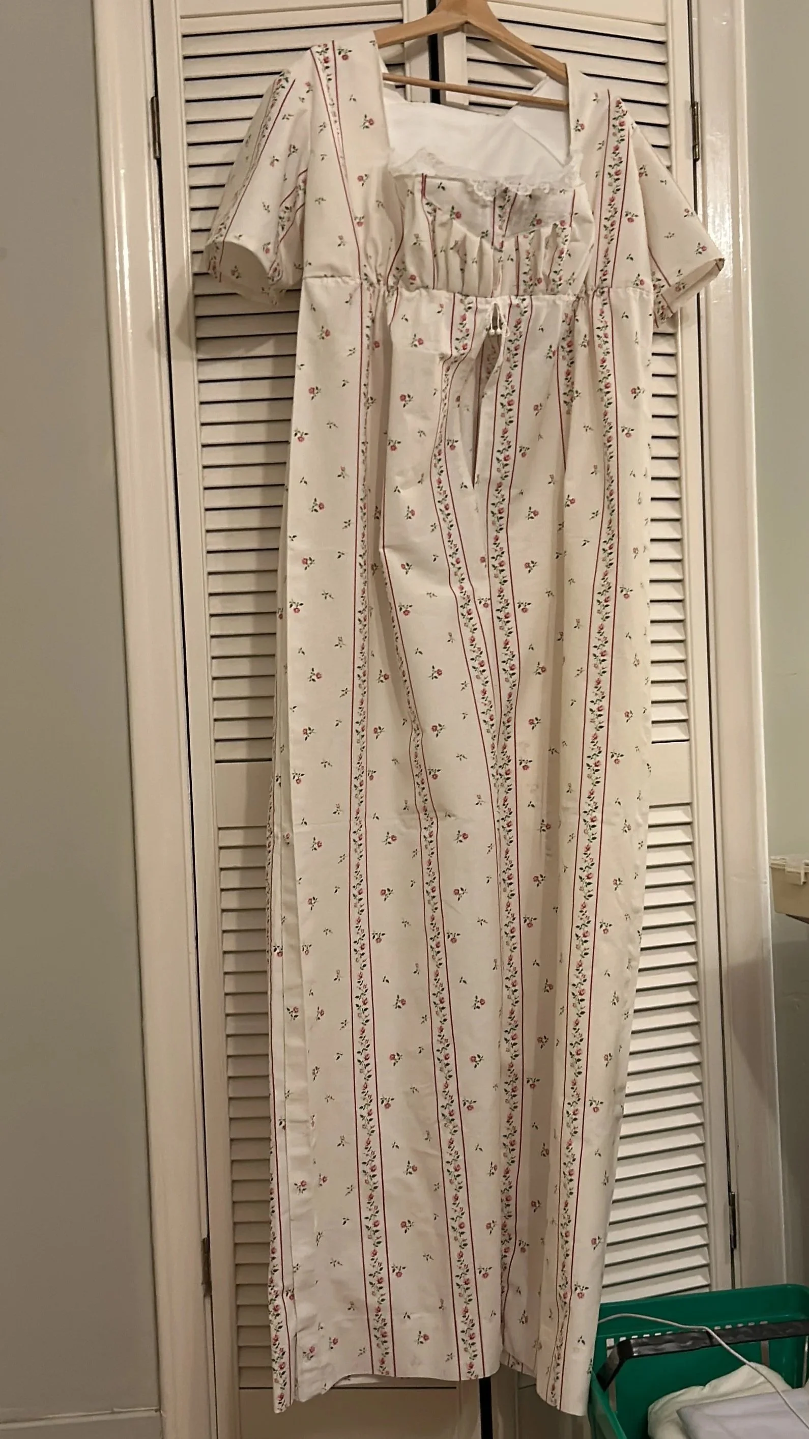 A long white dress with red and green floral patterns hanging on a wooden hanger.