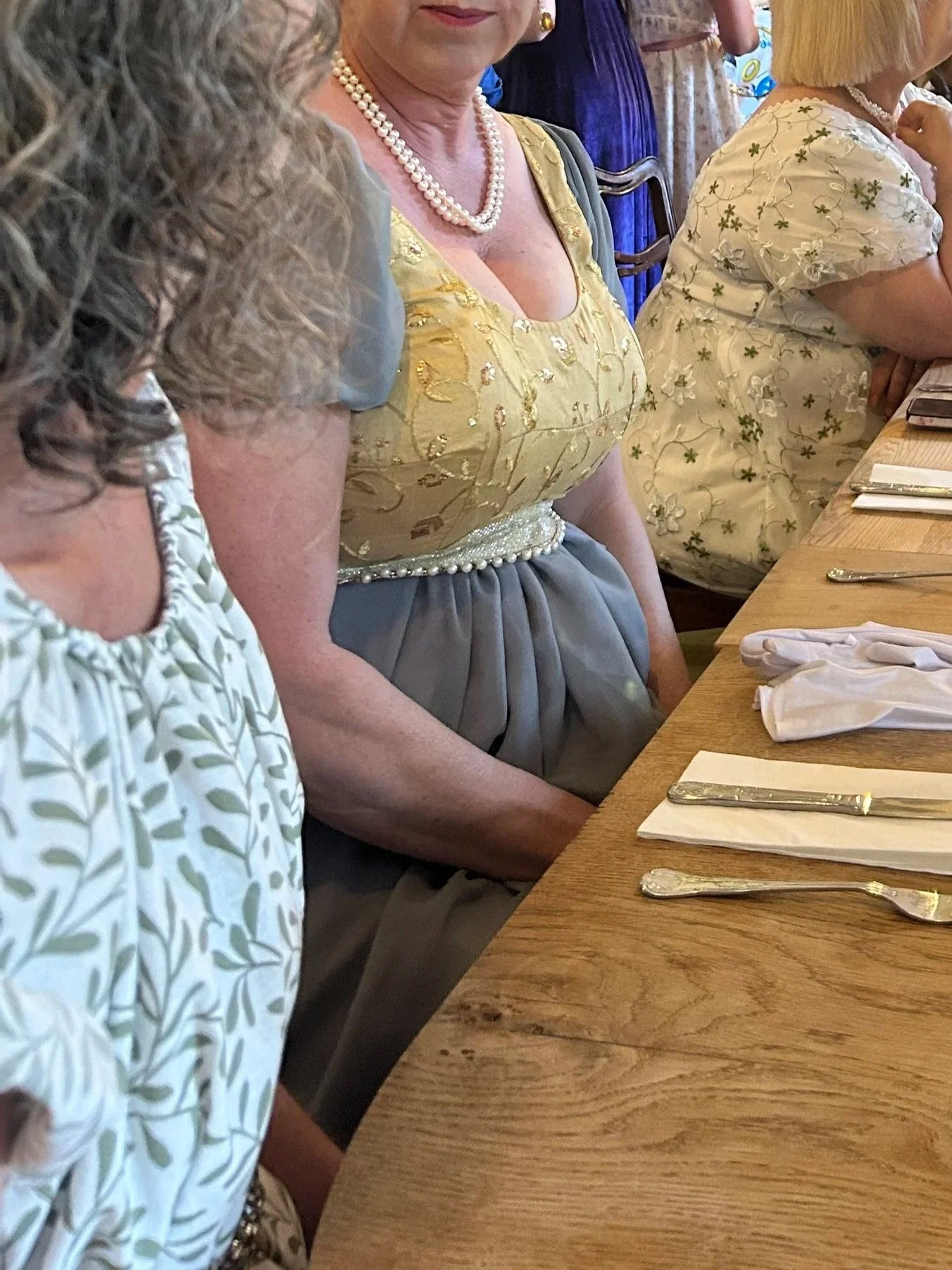 Women dressed in elegant clothing and pearl necklaces sitting at a restaurant table with silverware and napkins.