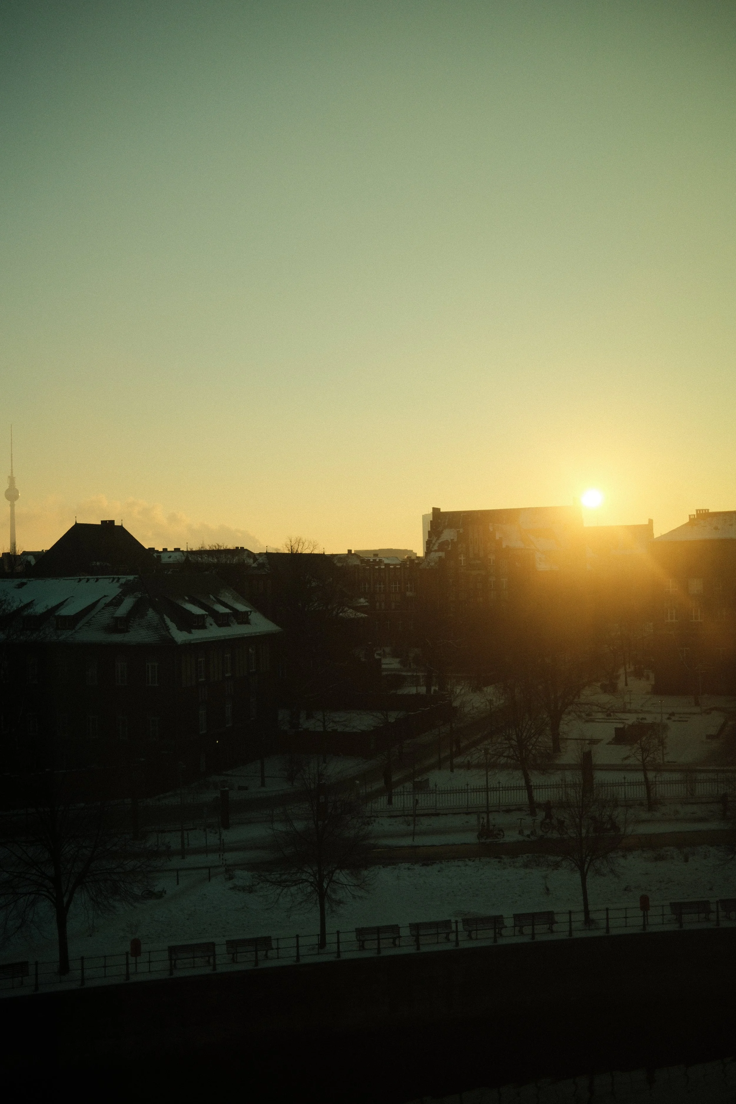 Sonnenaufgang über einem städtischen Winterlandschaft mit schneebedeckten Dächern und Bäumen.