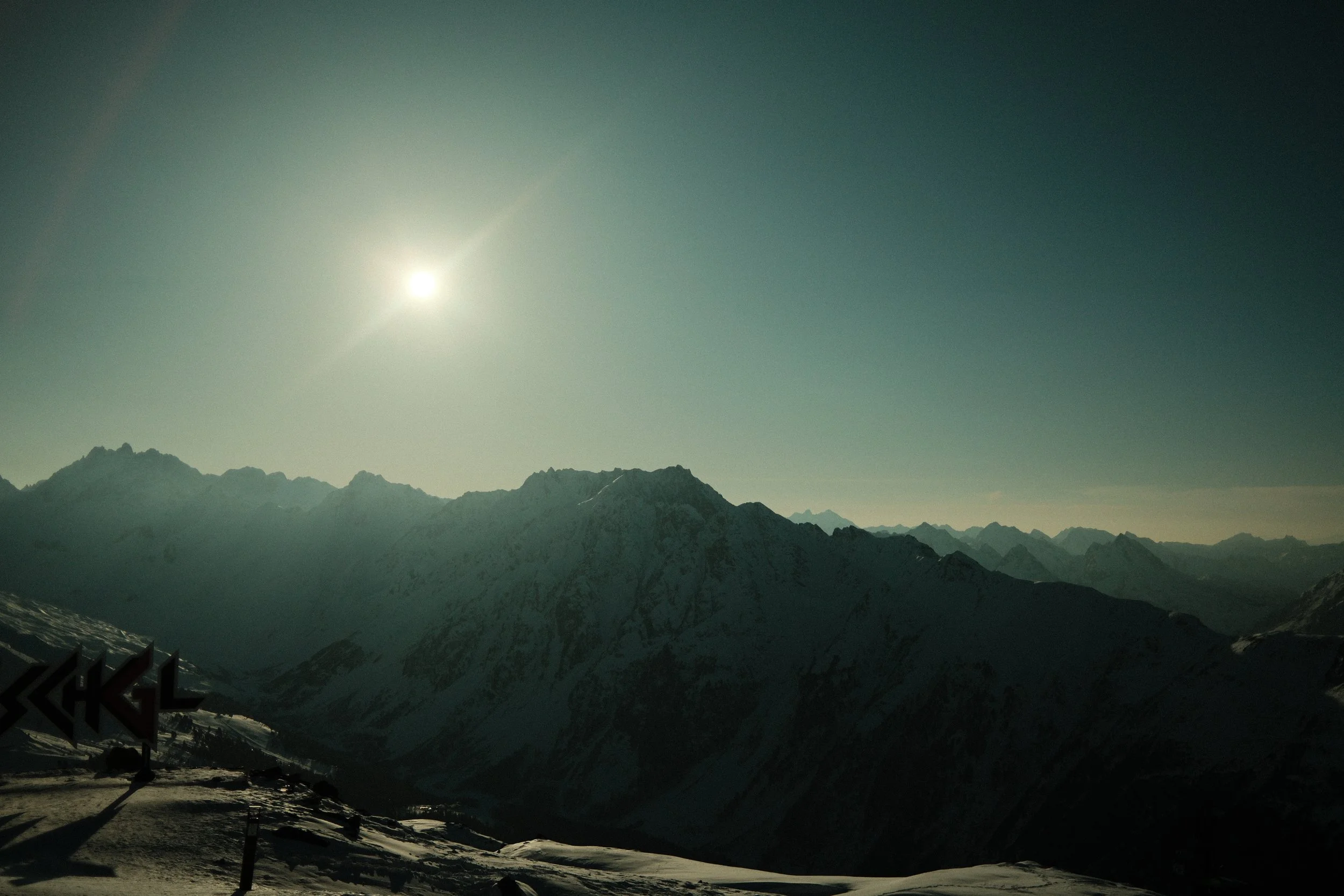 Berglandschaft mit schneebedeckten Gipfeln unter einem Himmel mit der aufgehenden oder untergehenden Sonne.
