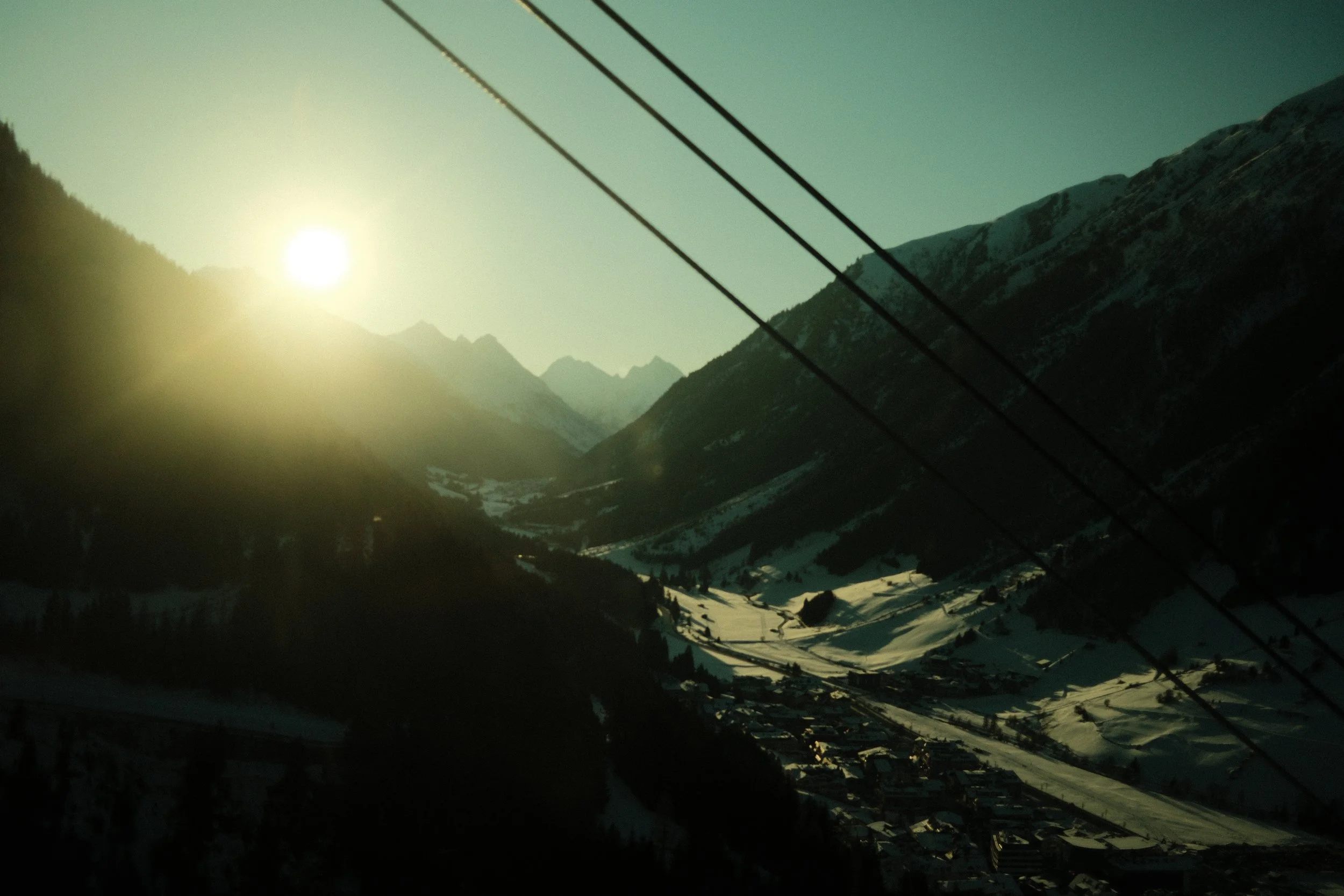Berglandschaft mit verschneiten Gipfeln, Sonnenlicht und Seilbahnseilen im Vordergrund