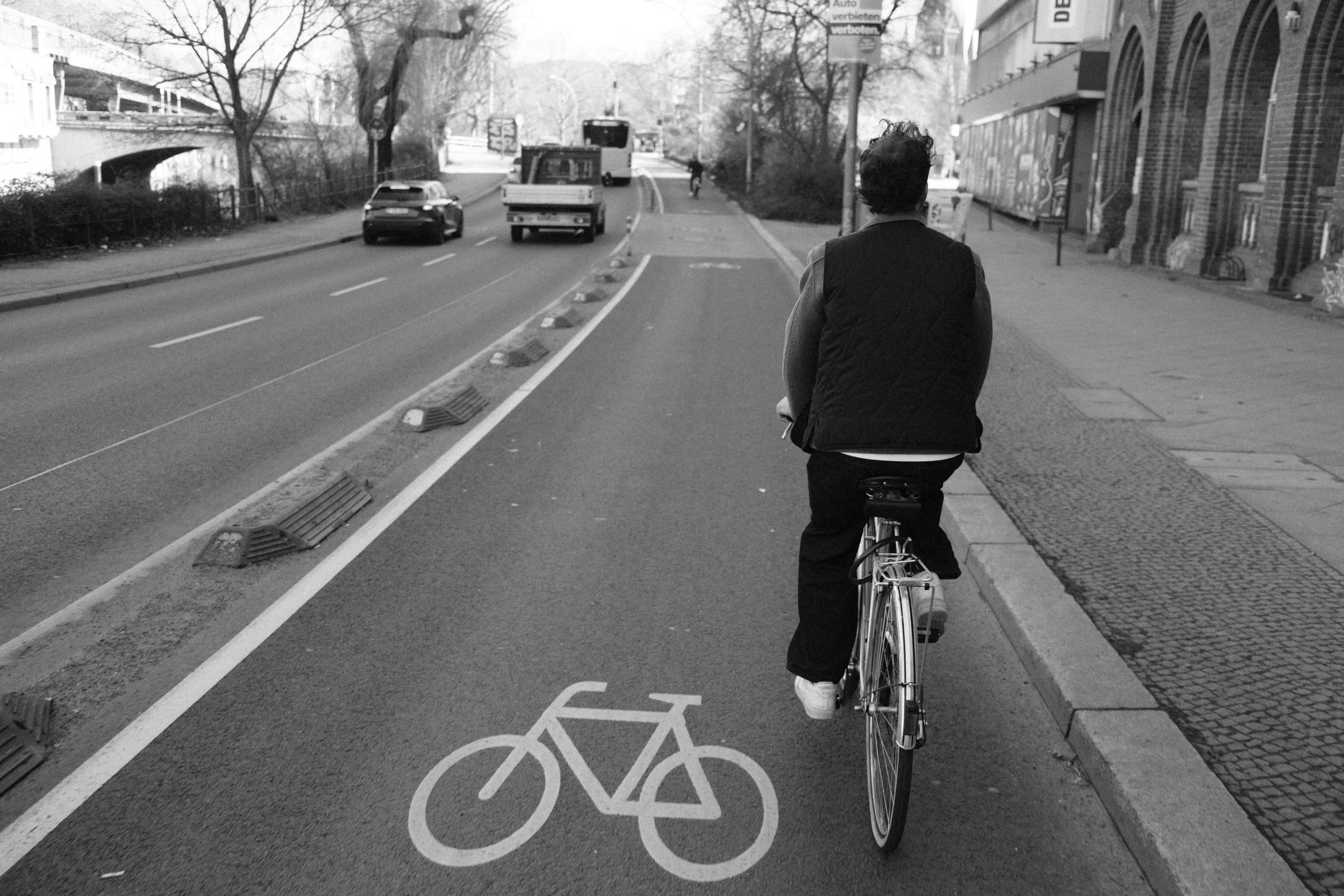 Eine Person fährt Fahrrad auf einem Fahrradstreifen, der durch eine weiße Fahrrad-Symbolmarkierung gekennzeichnet ist.