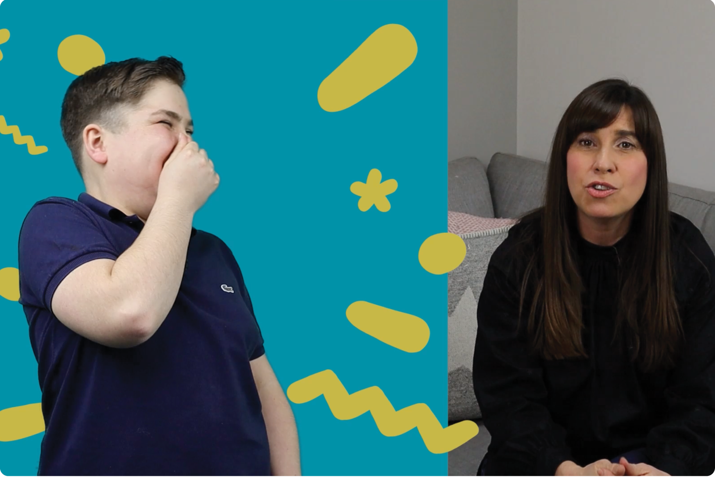 A boy in a navy shirt covering his mouth and laughing, next to a woman with long brown hair sitting in a room with a grey wall and grey chair.
