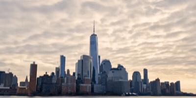 Skyline of New York City with One World Trade Center and other tall buildings under a cloudy sky.