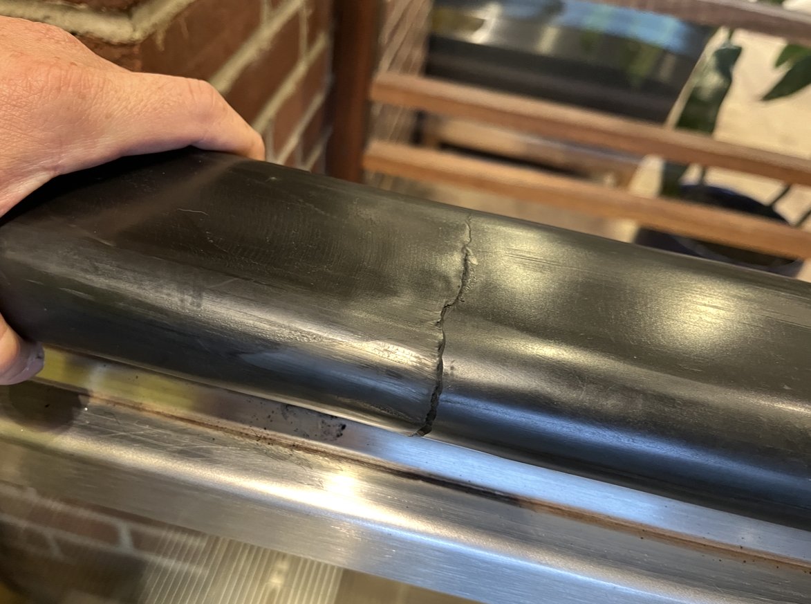 Close-up of a person holding a black, cracked pipe outdoors with a brick wall and wooden furniture in the background.