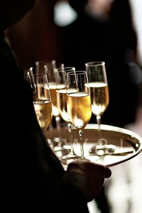 Person holding a tray with several glasses of champagne in a dimly lit setting.