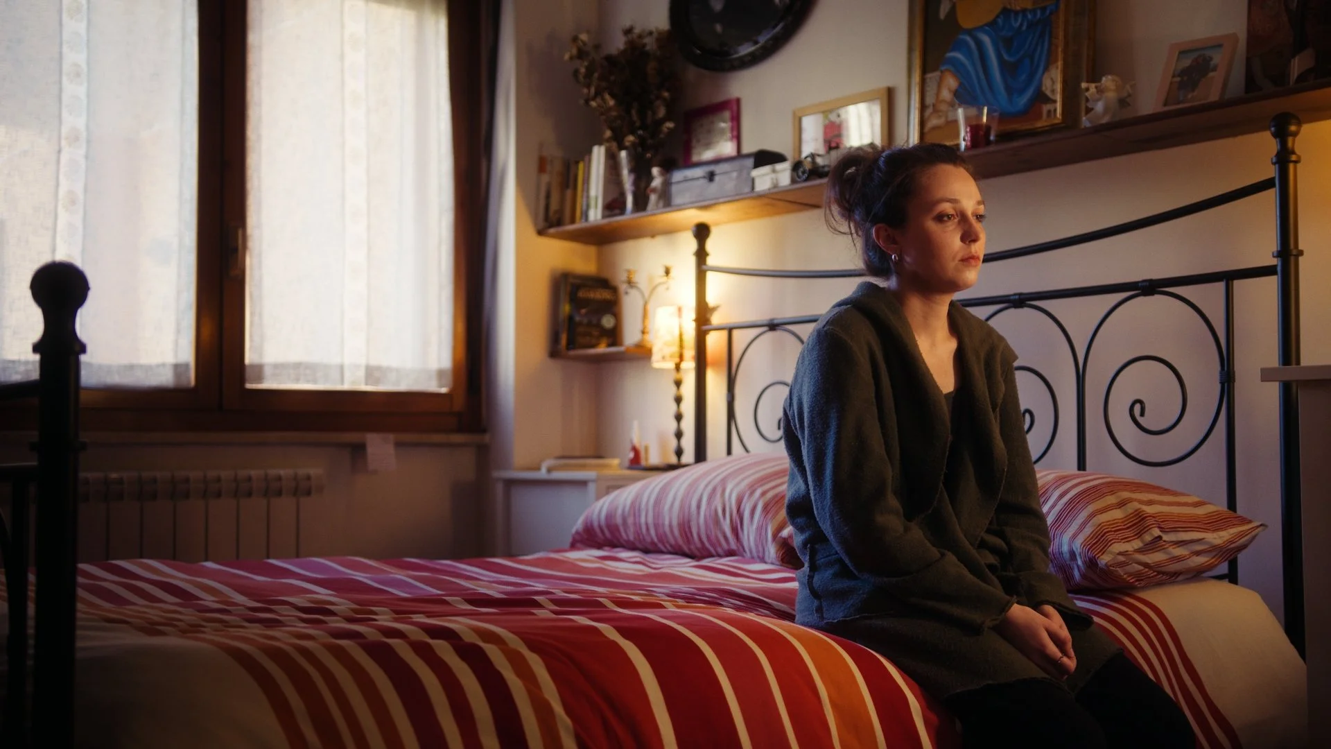 Woman sitting on a bed in a bedroom with daylight coming through a window