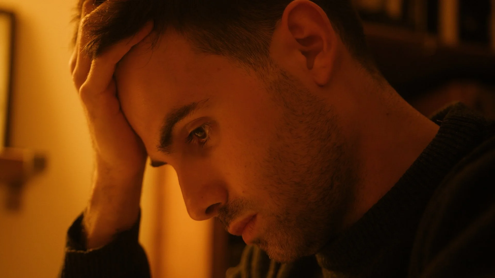 Man resting his head in his hand in a dimly lit room