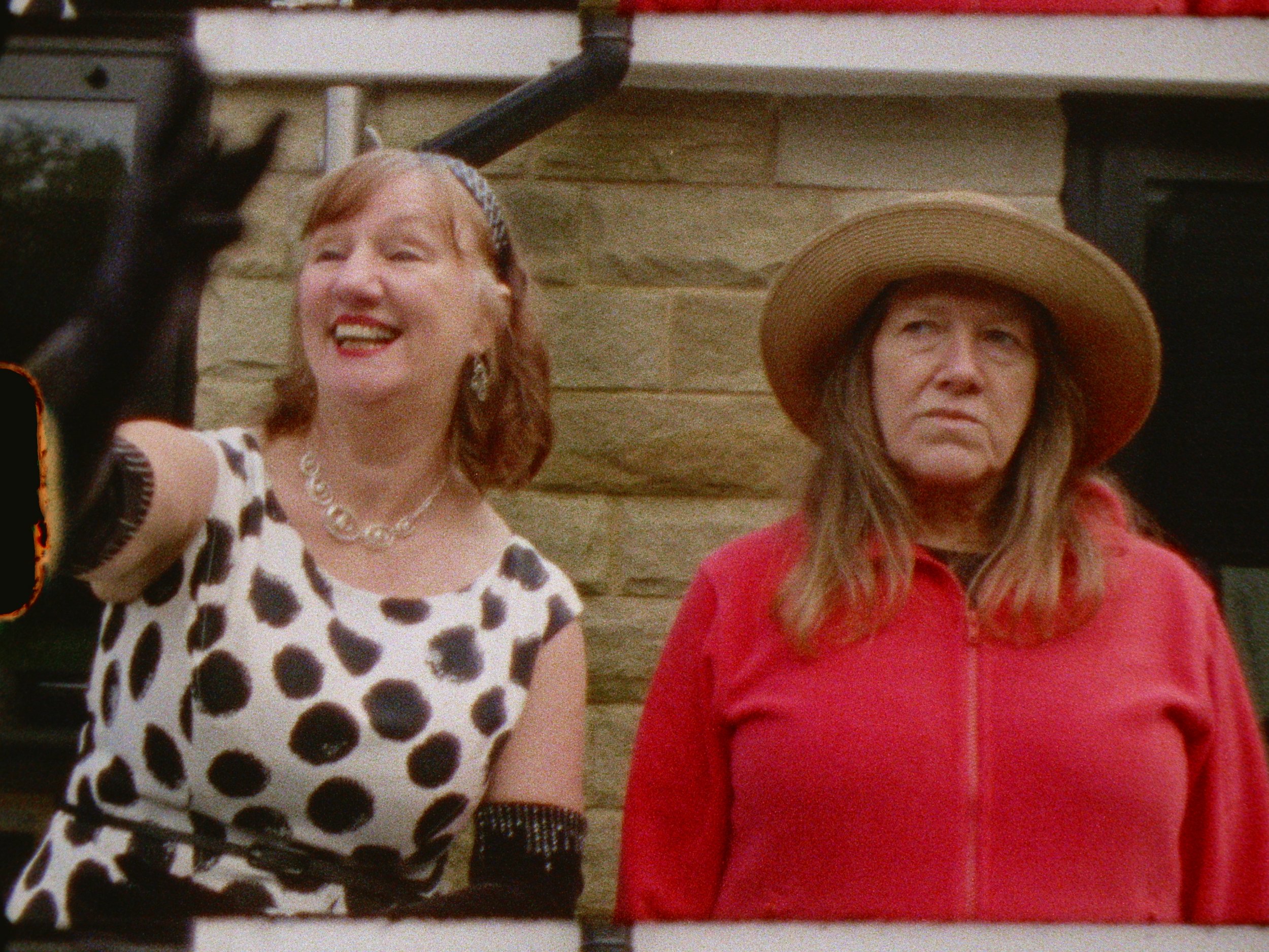 Two woman looking over a garden. One happy, the other angry
