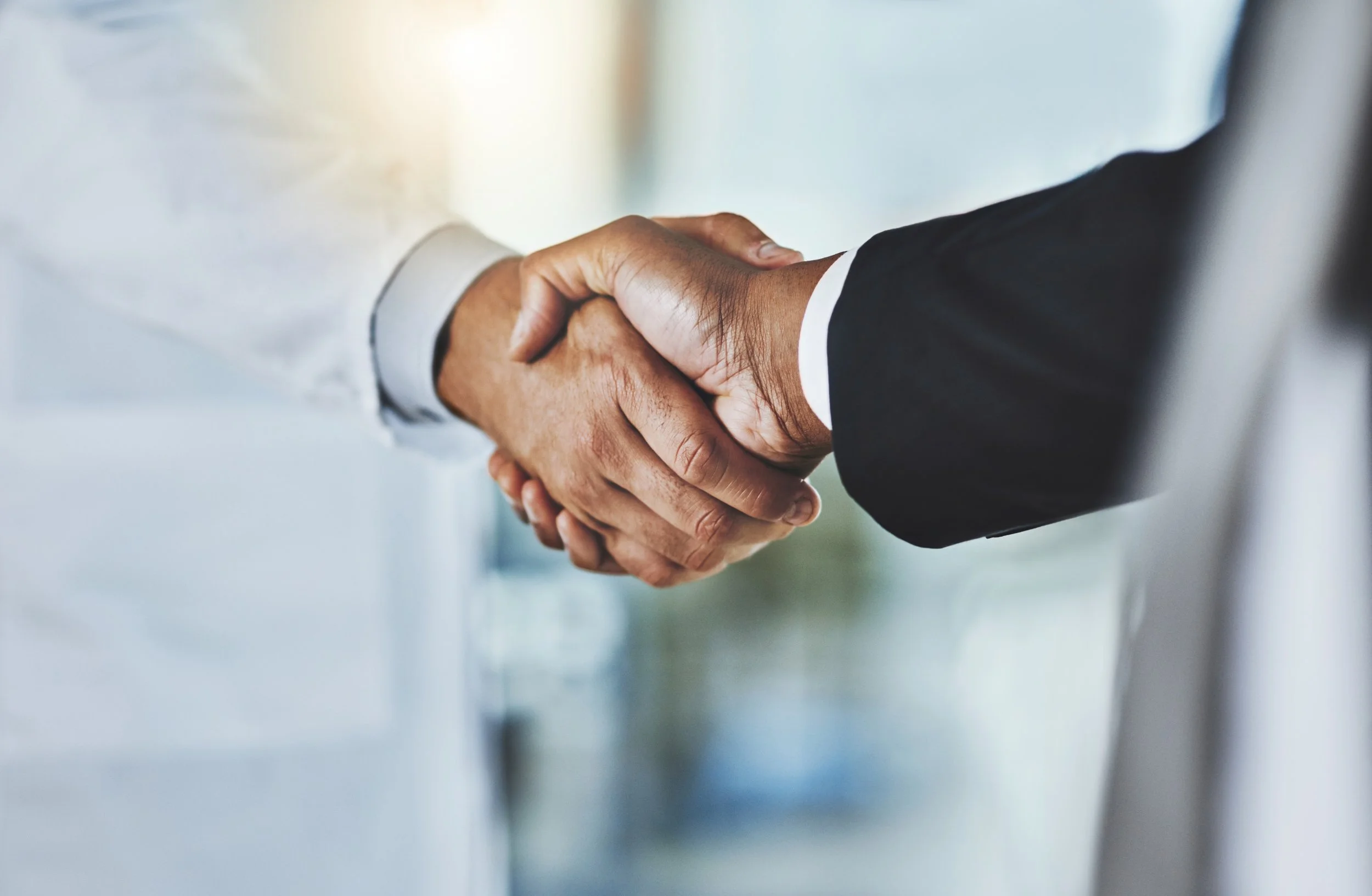 Close-up of two individuals shaking hands, one in a white shirt and the other in a black suit, symbolizing agreement or partnership.