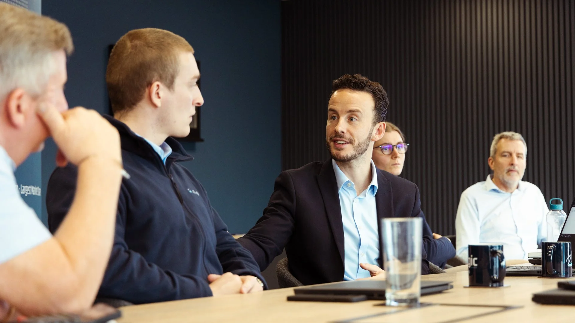 Group of five people having a discussion at a conference table in a modern office.
