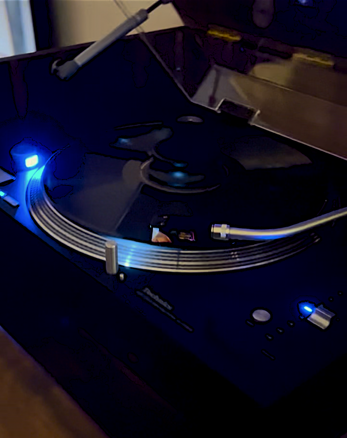Close-up of a turntable with a spinning vinyl record, illuminated by blue LED lights, showing the tonearm and controls.