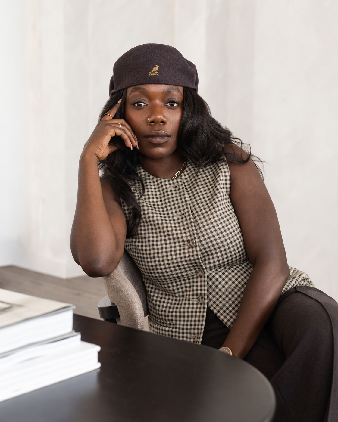 Sandra, consultante en organisation, assise à un bureau, coiffée d'un béret et vêtue d'un haut à carreaux, la tête appuyée sur sa main.