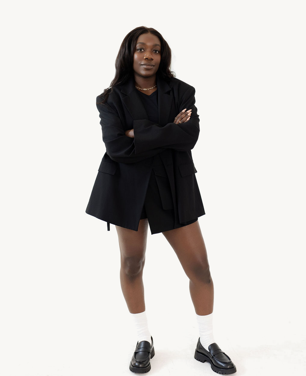 Sandra, consultante en organisation, debout, les bras croisés, en blazer noir sur fond blanc.