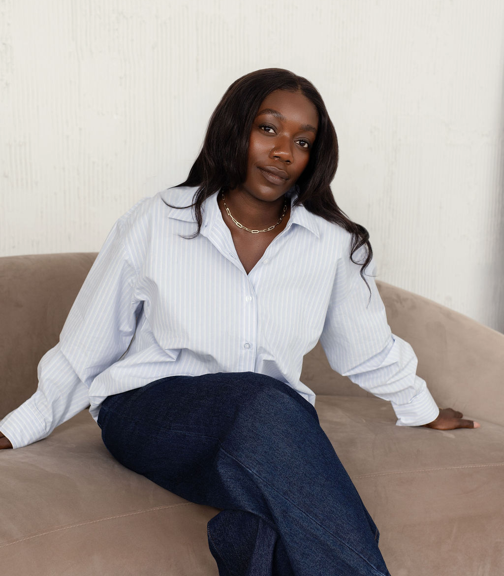 Sandra, consultante en organisation, assise sur un canapé beige, en chemise rayée et en jean.
