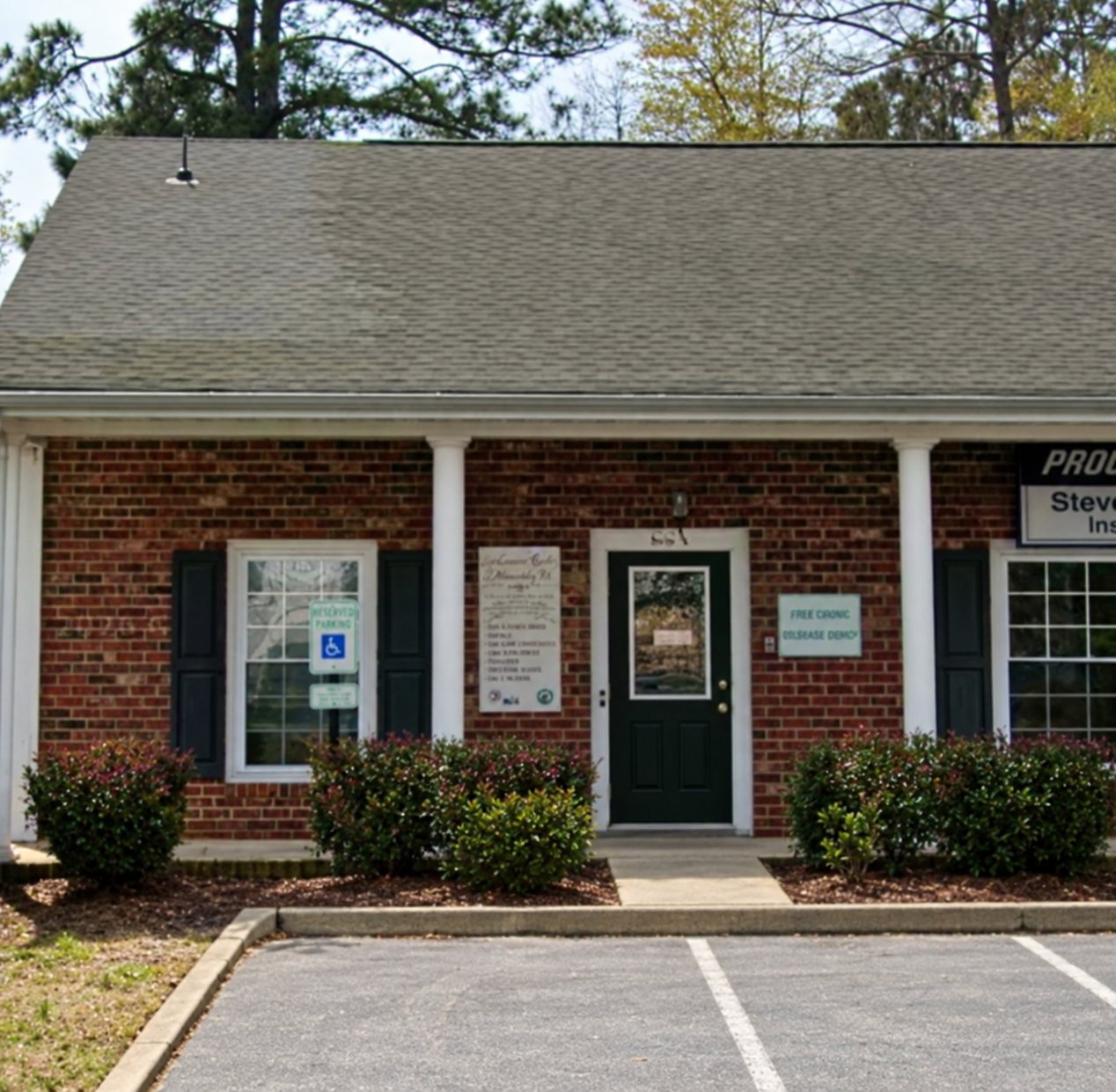Brick building with white columns and bushes in front, residential office signs, parking space in foreground.