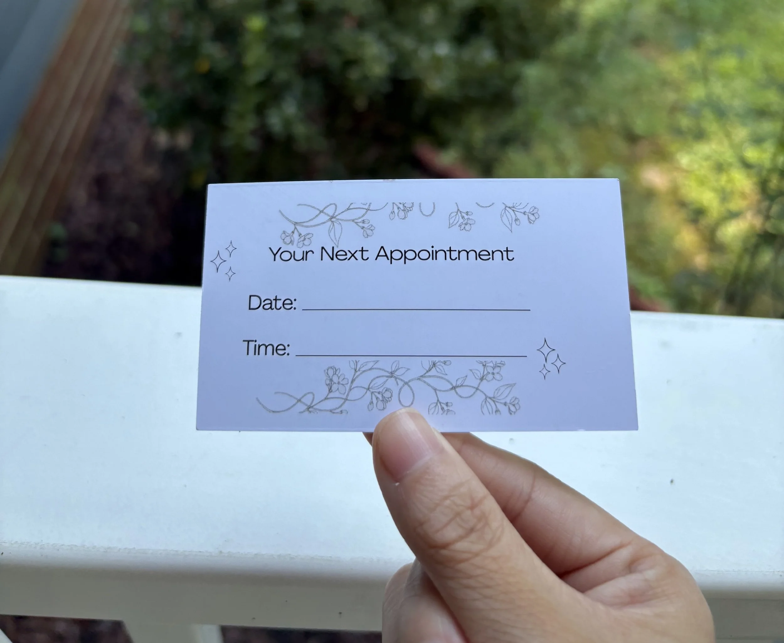 A person holding a card with the text "Your Next Appointment" and spaces for date and time. The card has floral decorative designs and small star-like icons.