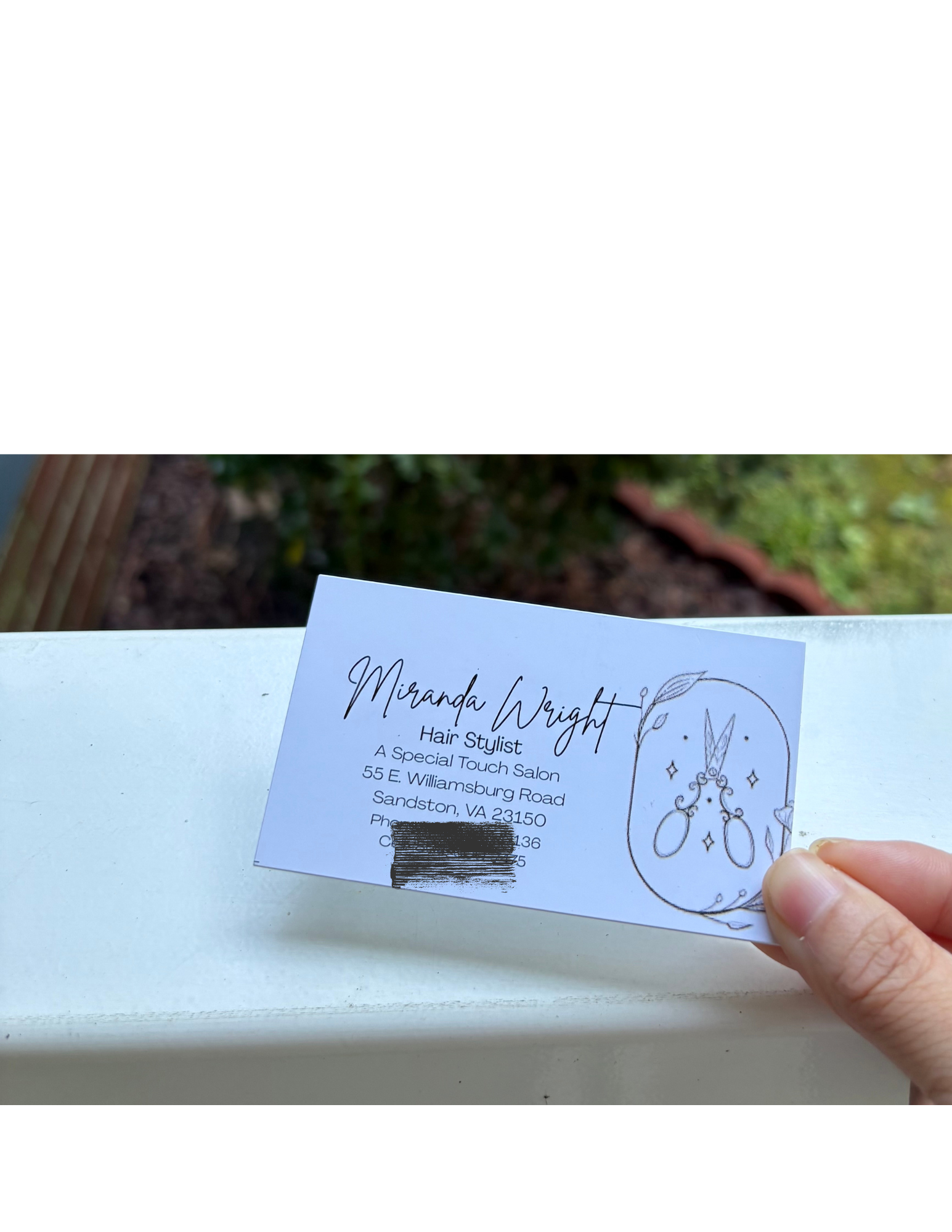 Close-up of a business card for Miranda Wright, a hair stylist at A Touch of Salon, with an illustration of jewelry and decorative elements, held by a person's hand.