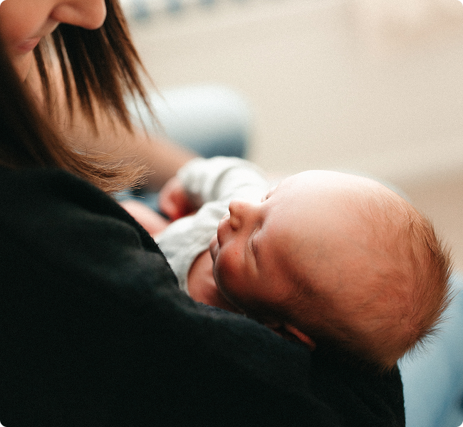 A woman holding a sleeping newborn baby close to her chest indoors.
